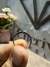 Close-up of a hand holding a ring with a blurred background featuring a plant and decorative items.