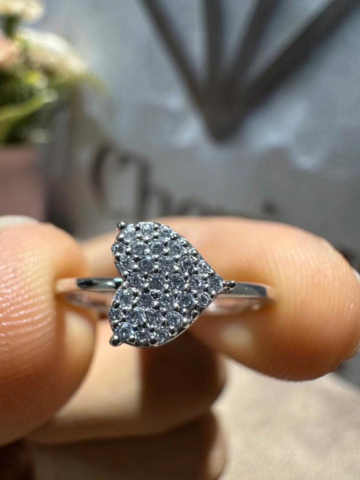 Heart-shaped silver ring with small stones held between fingers against a blurred background