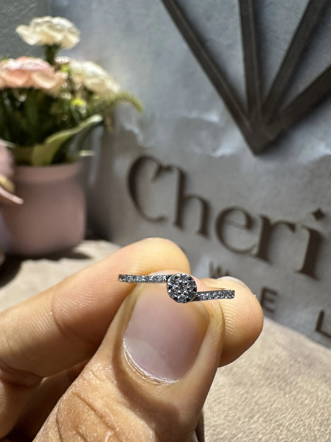 Diamond ring held between fingers with 'Cheri' branding in the background
