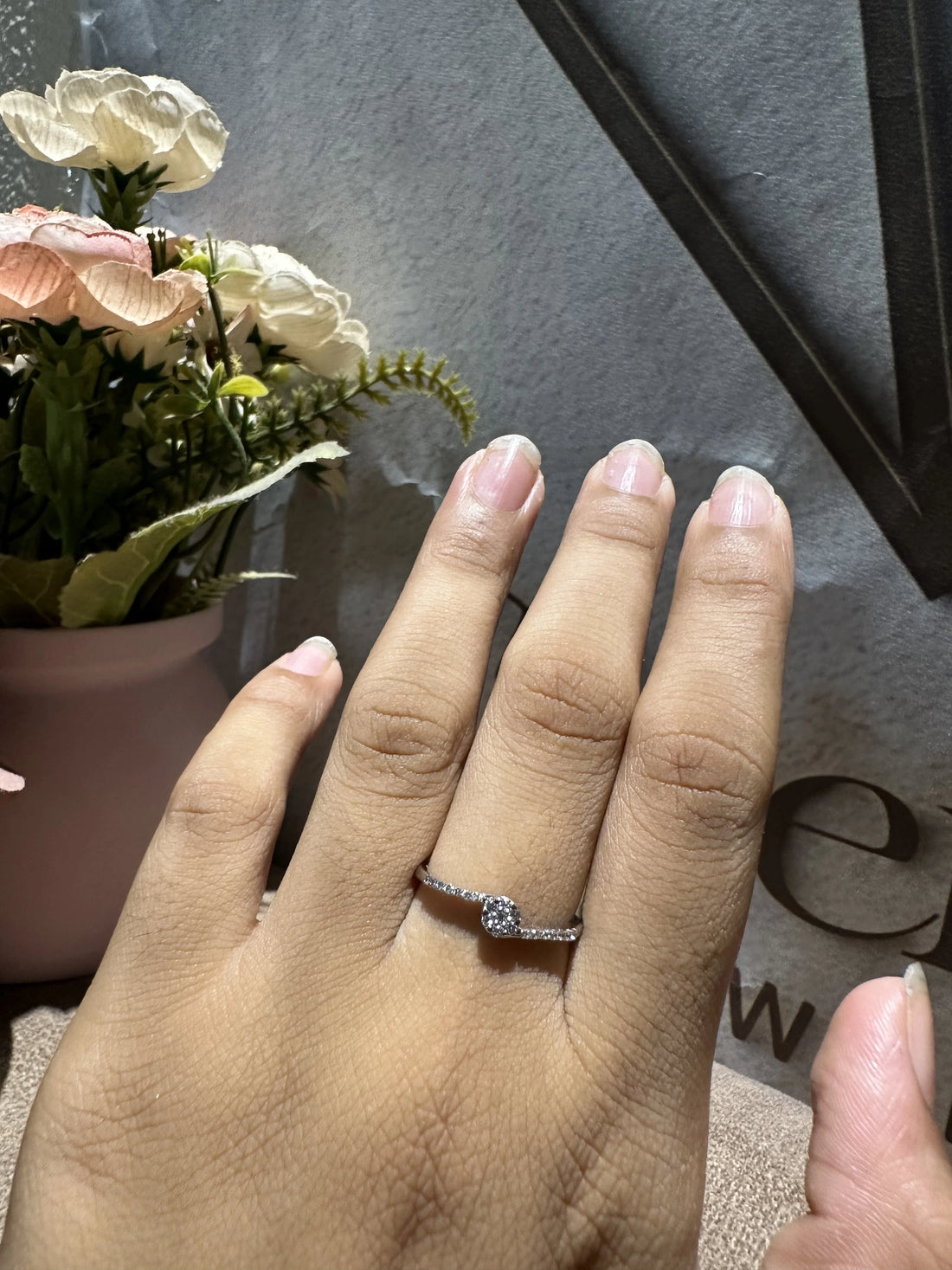 Hand wearing a ring with flowers and a black frame in the background