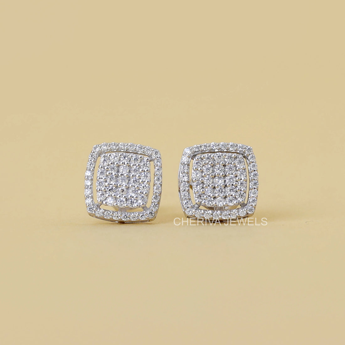 Pair of diamond earrings on a beige background with 'CHERIVIA JEWELS' branding.