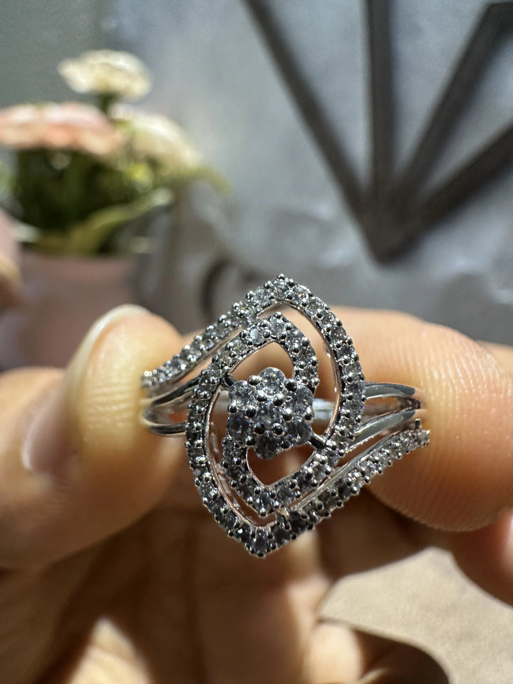 Silver ring with heart design held between fingers against a blurred background